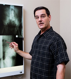 Dr. Howell, chiropractor standing at a light board examining x-rays wearing a dark colored button up shirt.