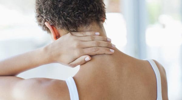 Woman holding the back of her neck, illustrating apparent neck discomfort.